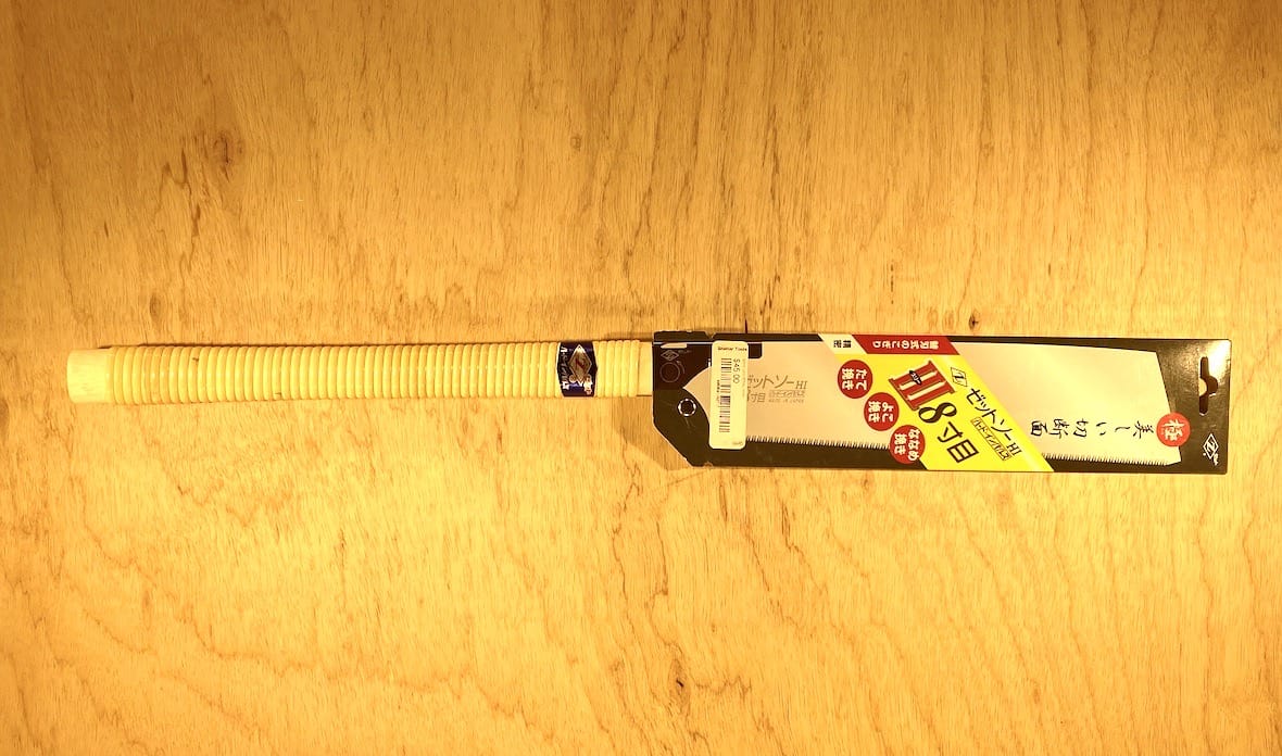 A Universal Saw 250 III by MARU, featuring Japanese text on its packaging, rests on a wooden surface beside an exquisite fine woodworking project.