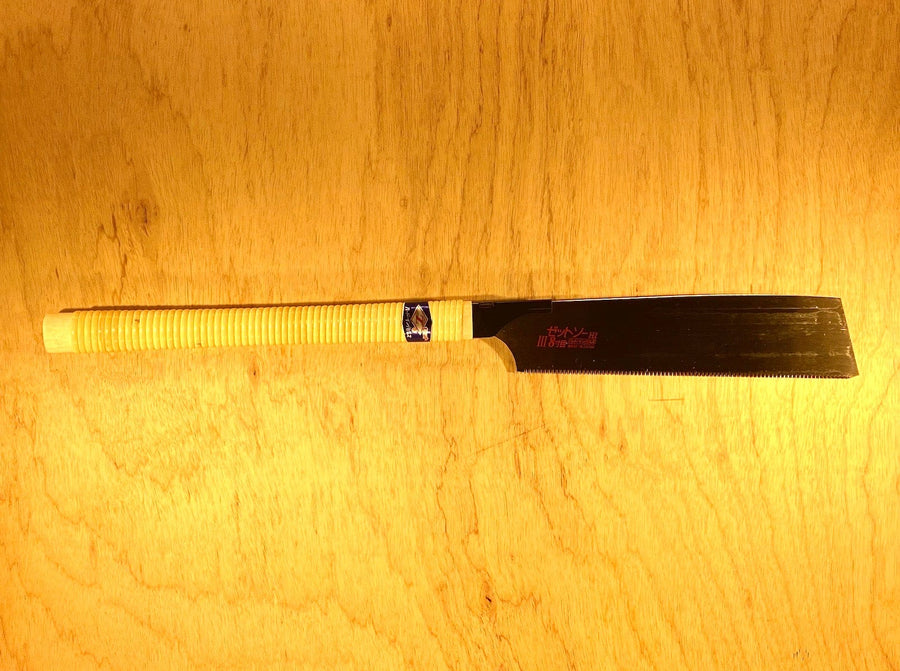 The Universal Saw 250 III by Z-Saw, a Japanese pull saw from the MARU brand, with a wrapped handle and a straight, thin blade featuring universal teeth, is placed on a wooden surface.