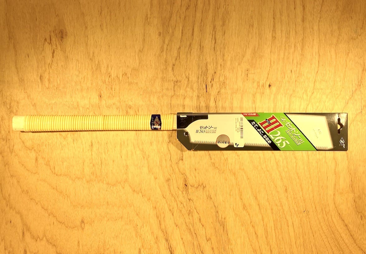 A Z-Saw Universal Saw 265 by MARU with a green label rests on a wooden surface, reminiscent of a versatile cutting tool with chisel-like teeth.