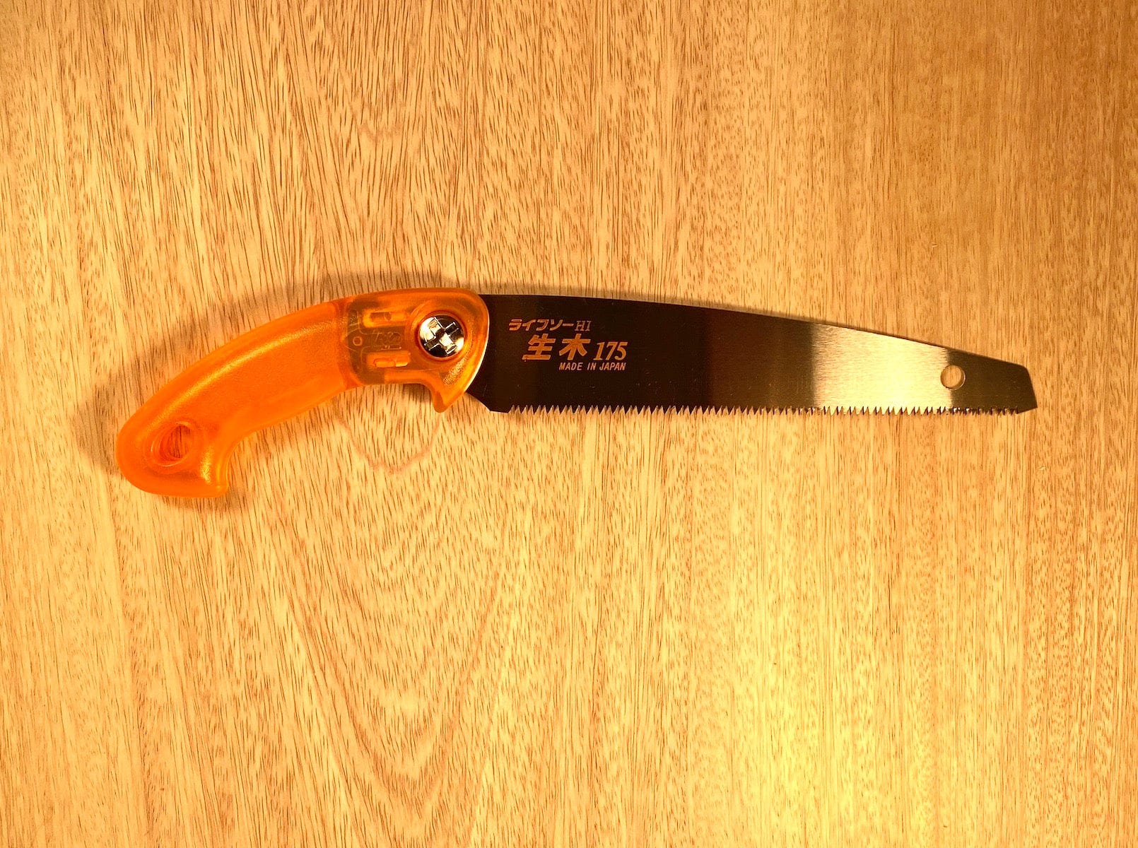 The Z-Saw Universal 175, a sharp Japanese pull-saw by MARU with an orange handle, lies on wooden planks, poised for garden maintenance.