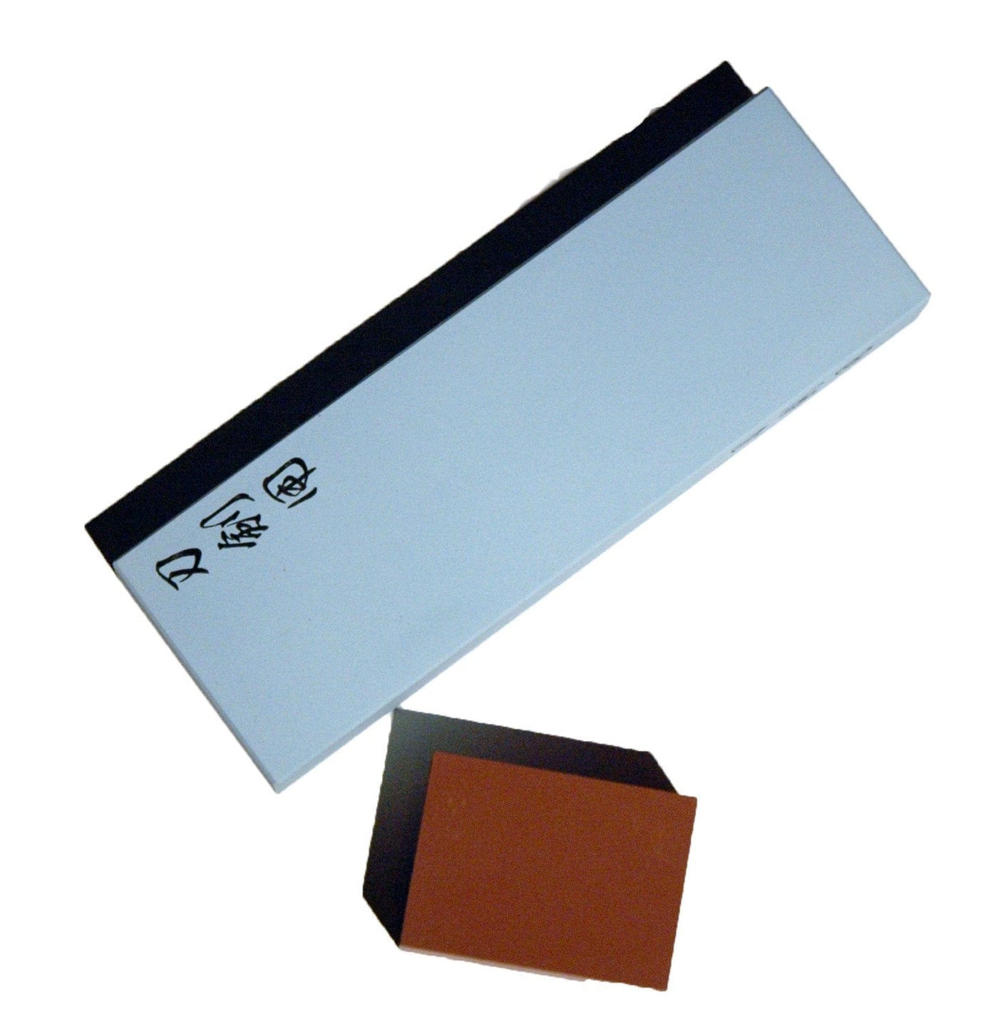 A MARU 10,000 Grit Ceramic Water Stone, with one side white adorned with black Japanese characters, and a smaller Nagura Stone positioned below it.