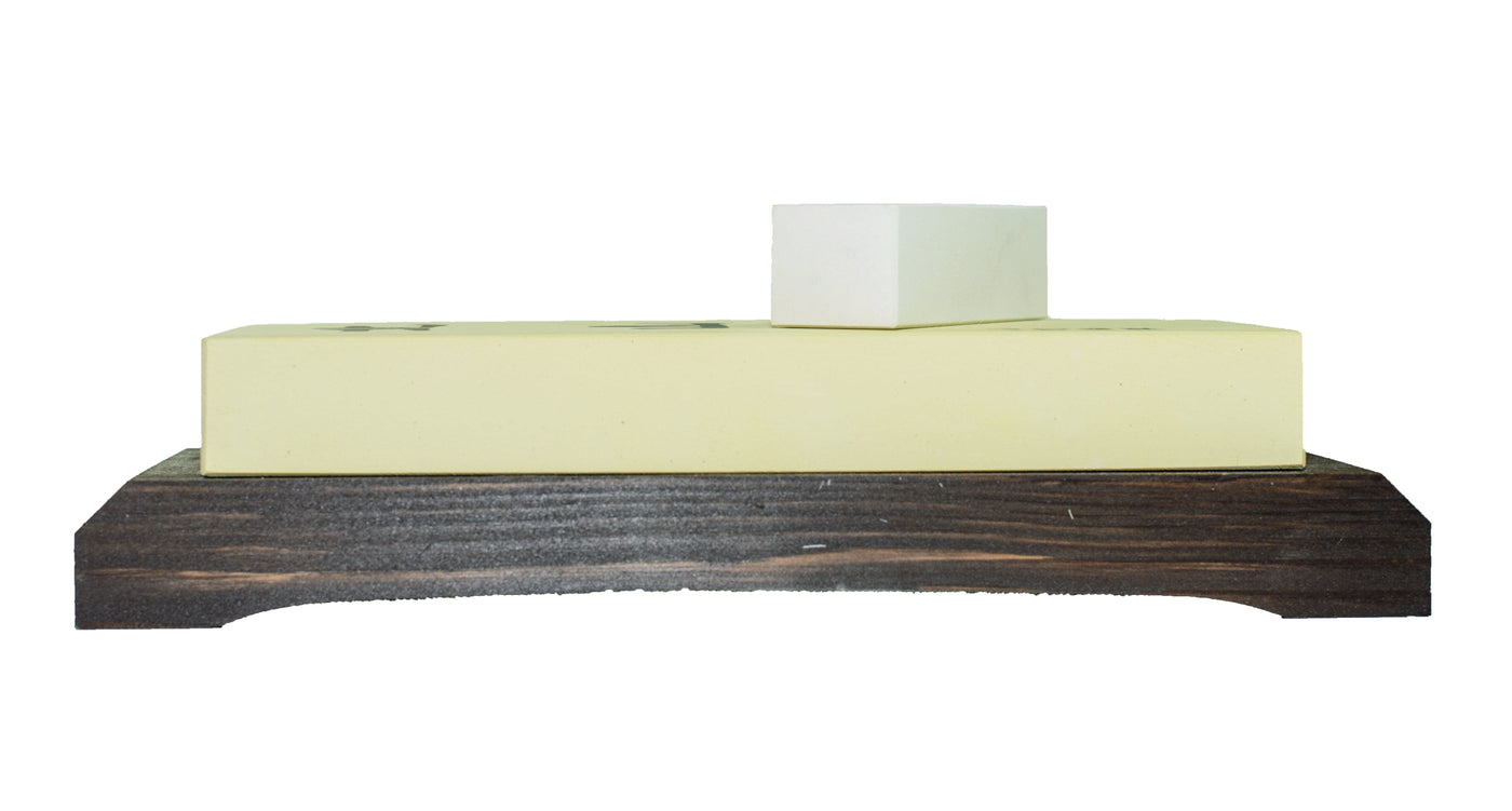 Two rectangular stones from MARU, an 8000 Grit Kitayama Stone set, are stacked on a dark wooden stand. The larger stone is yellow and crafted with natural stone powder, while the smaller one is white.
