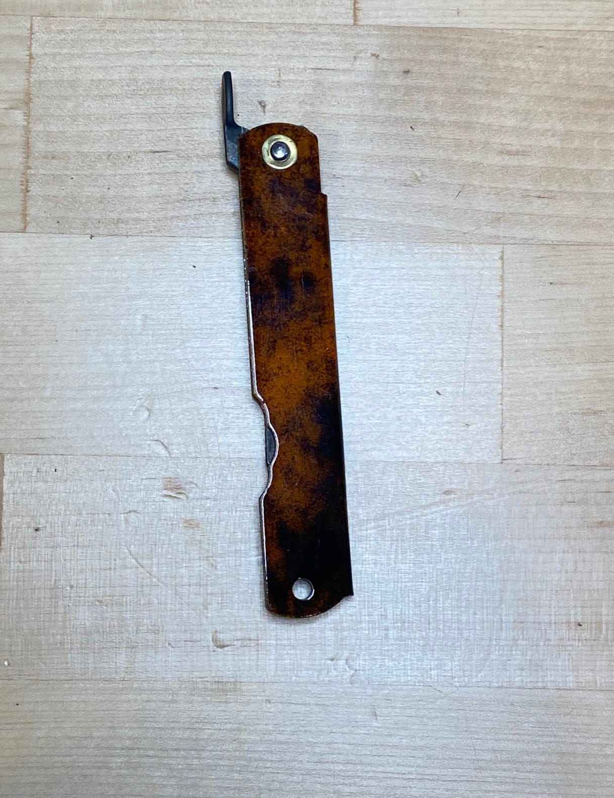 A heavily used, rusted MARU Higonokami Folding Knife Large Blue Steel Blade from Japan lies on a light wooden surface, its hooked end and bolt near the tip evoking rugged character and vintage craftsmanship.