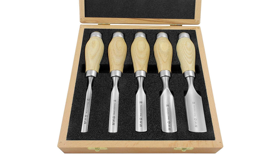 The MHG Firmer Gouge Set includes a wooden box containing five chisels, each equipped with durable alloy-steel blades and wooden handles. This essential set of woodworking tools is neatly organized on a foam insert, with each chisel clearly labeled by size for easy identification.