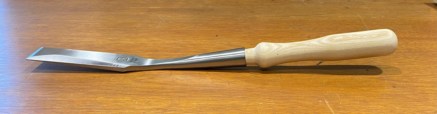 Introducing the MHG Timber Framing Slick, a top-notch woodworking tool by MHG, equipped with a high-alloy metal blade and a wooden handle, ideal for slick timber framing projects and elegantly showcased on a wooden surface.