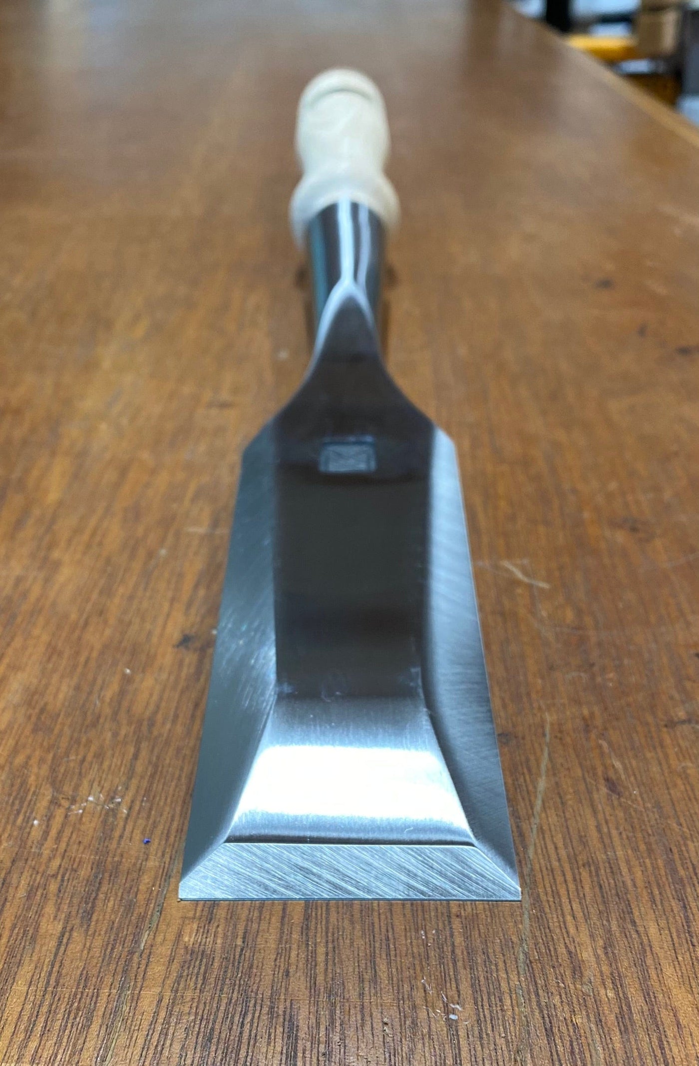 A close-up of a finely crafted woodworking tool, the MHG Timber Framing Slick, features its wooden handle resting gracefully on a timber surface, showcasing the precision of this MHG creation.