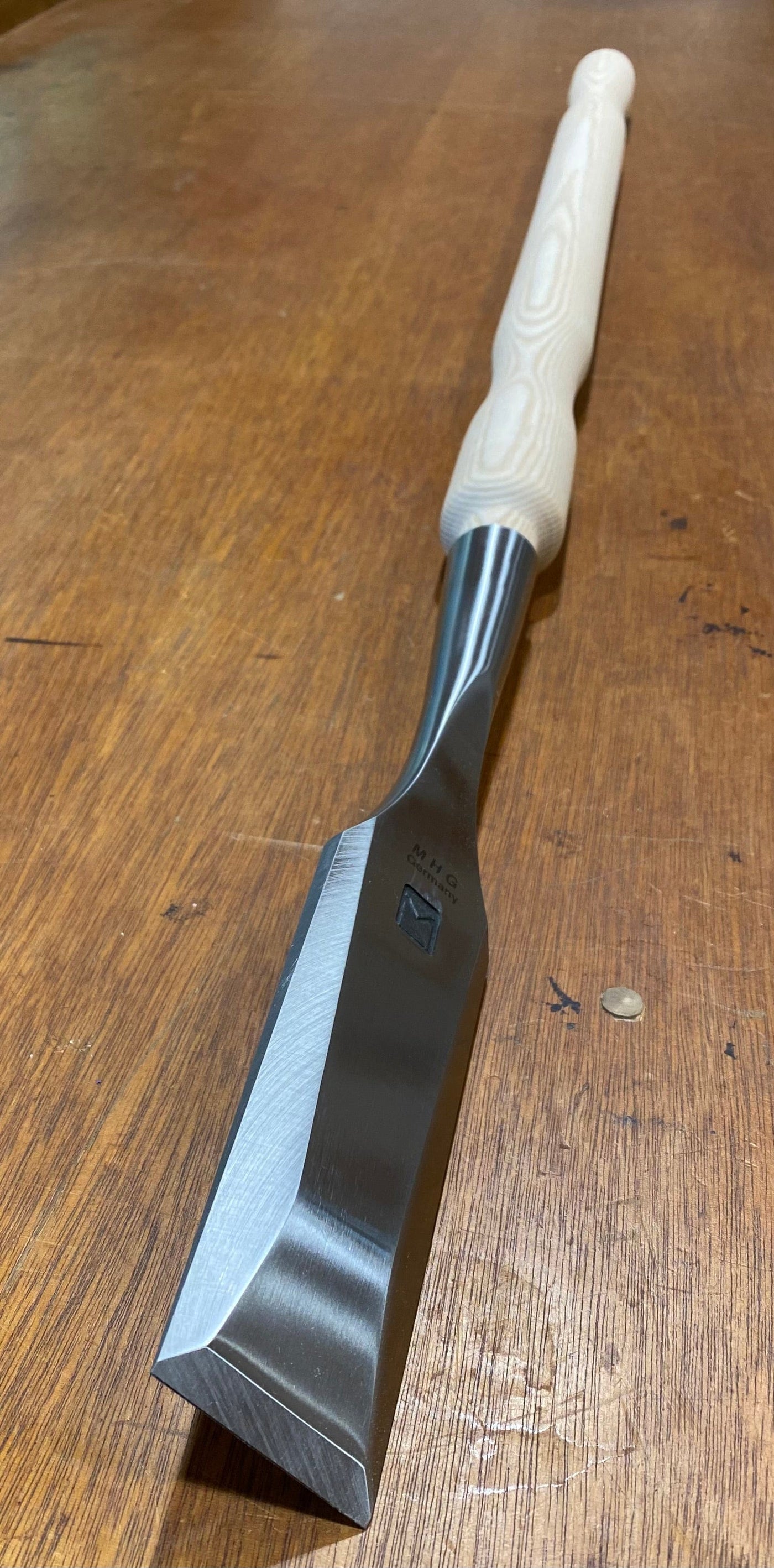 Close-up of the MHG Timber Framing Slick, featuring a light wooden handle and crafted from high-alloy material, lying on a wooden surface.