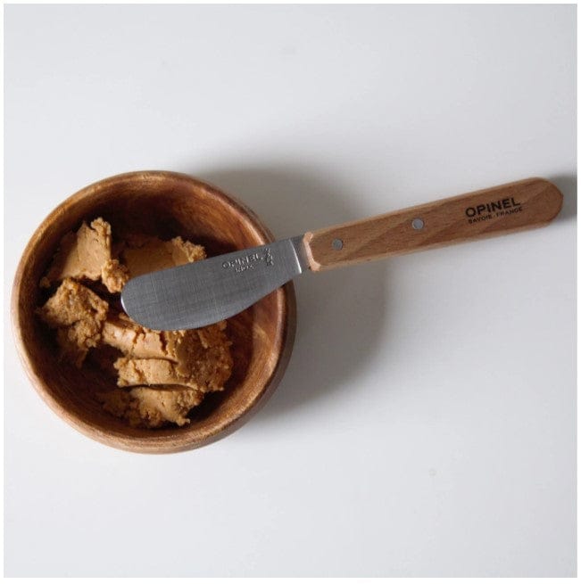 A wooden bowl with beige paste is paired with the Opinel Essential Spreading Knife, featuring a wooden handle and high carbon stainless steel blade.