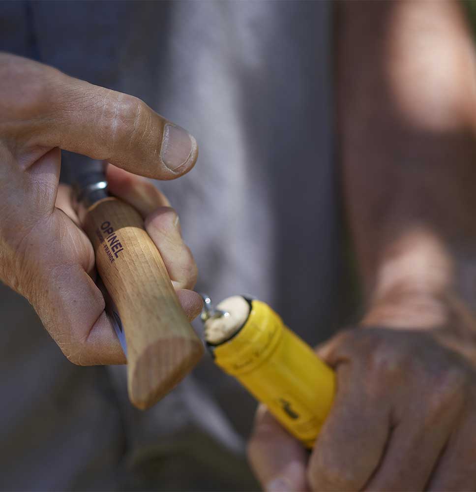 An individual is holding the Opinel Knife with a wooden handle featuring a professional-quality corkscrew and cheese knife, along with a yellow cylindrical object, possibly joining or adjusting them.