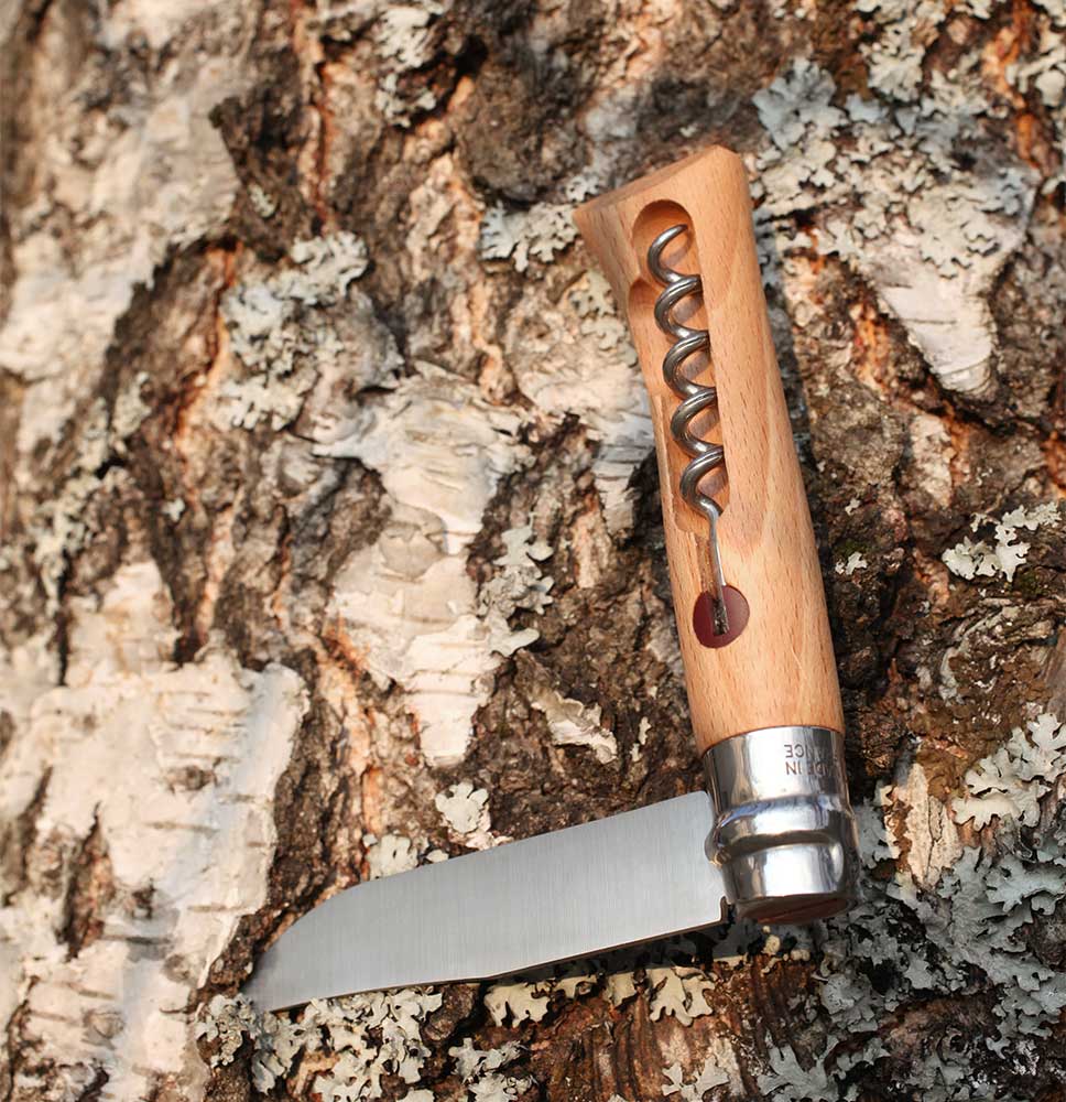 An Opinel Knife Opinel Corkscrew and Cheese Knife with a professional-quality stainless steel corkscrew handle is stuck into the bark of a tree.