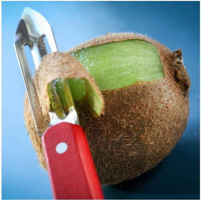 A close-up of a kiwi being peeled with the Opinel No.115 Micro-Serrated Stationary Peeler, featuring a red handle and micro-serrated blade—perfect for chefs needing precise results as it reveals the green flesh beneath the brown skin.