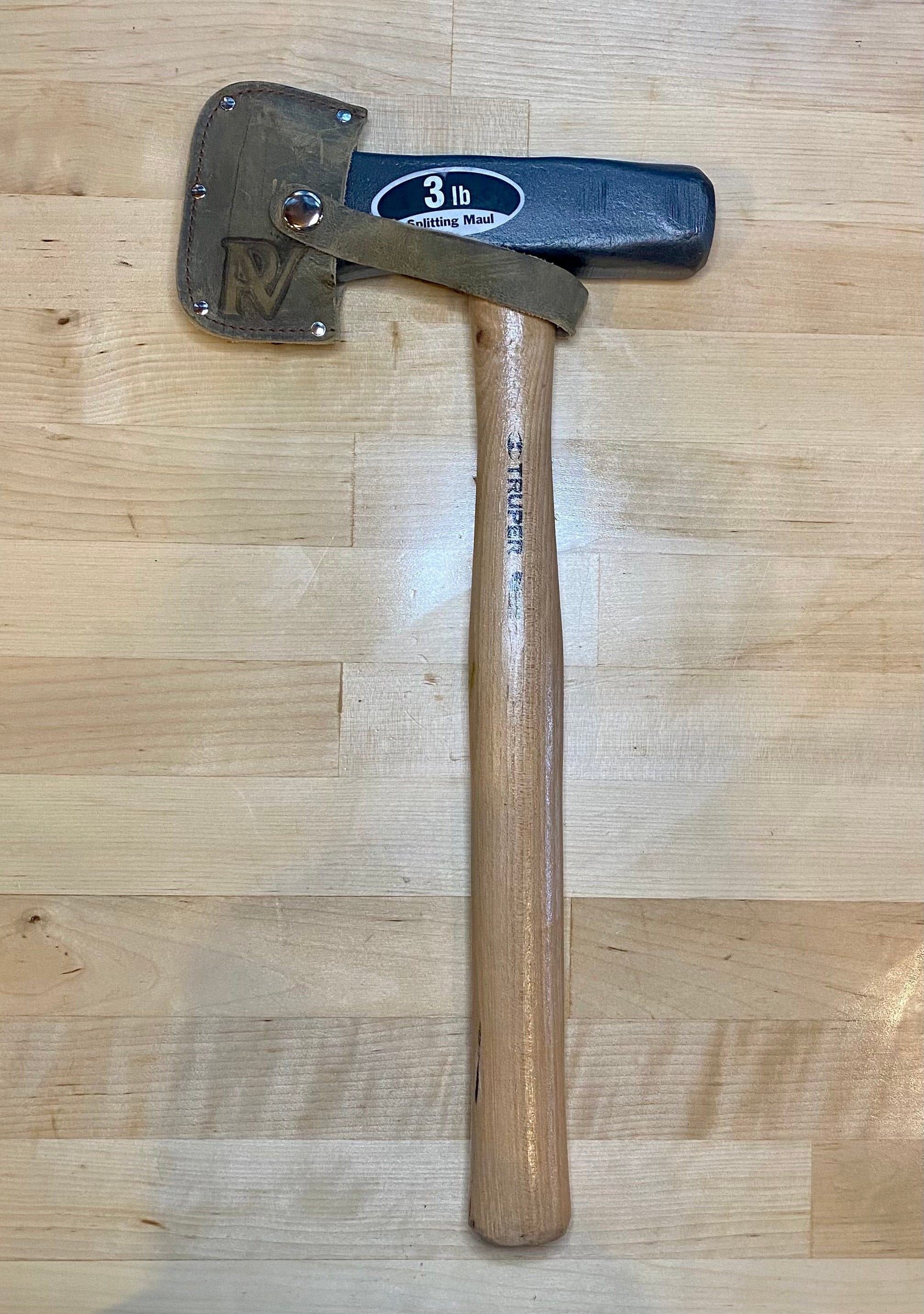 The PEA Peavey Mini Splitting Maul, featuring a 3-pound black metal head, protective leather cover, and wooden handle, rests on a light wood surface—ideal for outdoor use or as part of your camping gear.