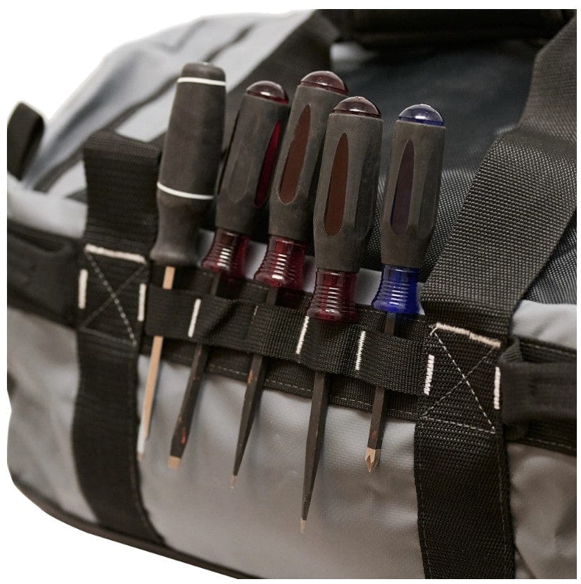 A set of black-handled screwdrivers fits into side slots of the rugged PUL Shelter Institute Duffel, crafted from waterproof tarpaulin.
