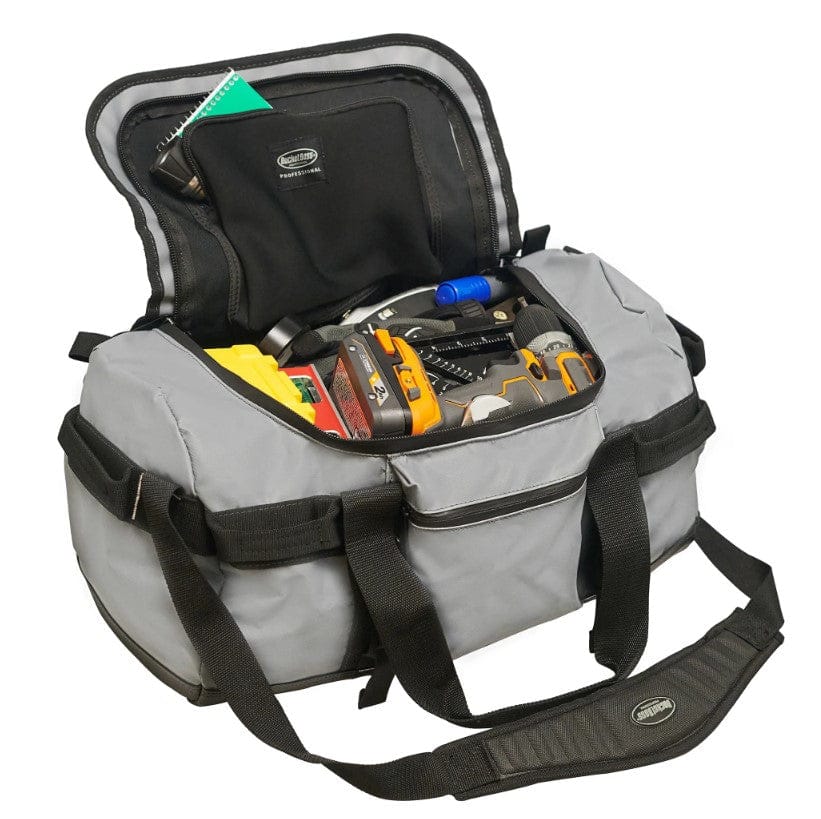 The Shelter Institute Duffel by PUL is a gray, open-top tool bag made from waterproof tarpaulin, featuring visible black straps and handles. Inside, it displays various tools like a cordless drill and measuring tape, ensuring durability in any condition.