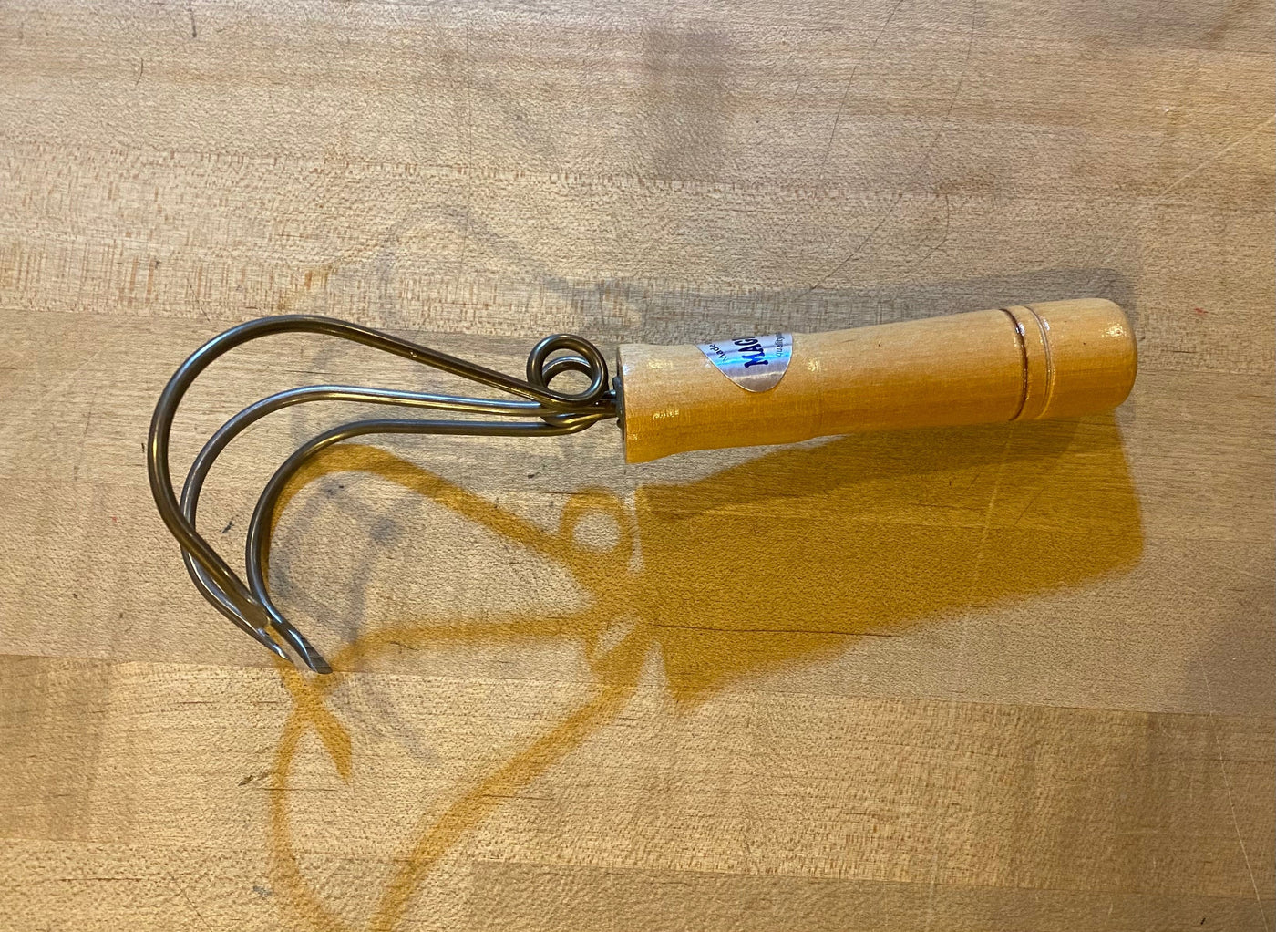 The QMT Magic Weeder Gardening Tool, featuring a wooden handle and three prongs, rests gracefully on a wooden surface, offering an ideal weeding solution.