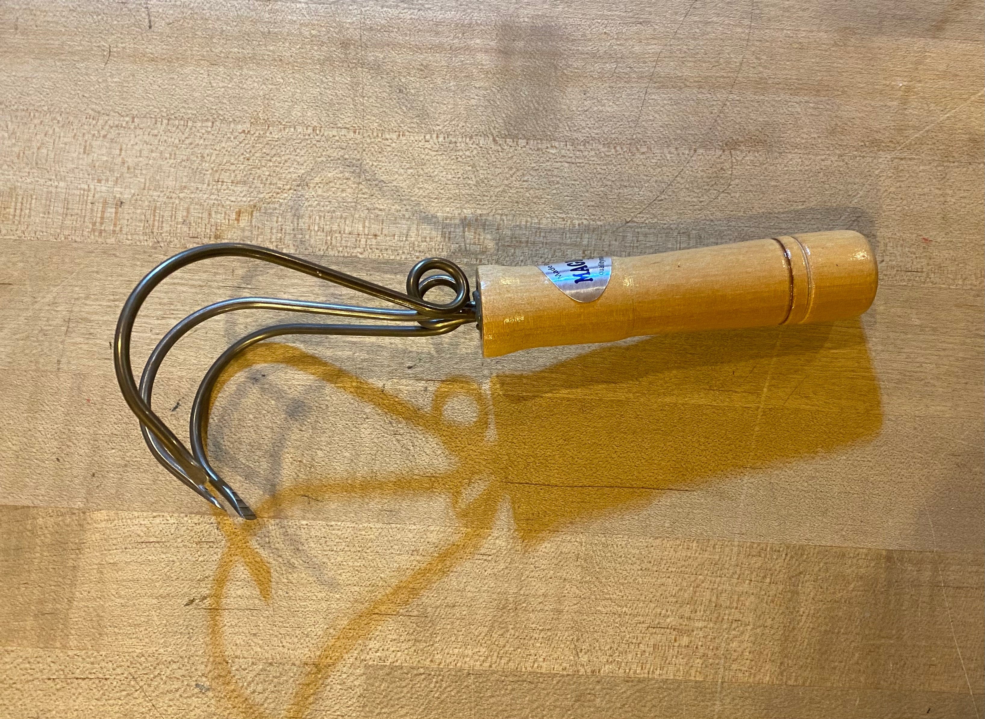 The QMT Magic Weeder Gardening Tool, featuring a wooden handle and three prongs, rests gracefully on a wooden surface, offering an ideal weeding solution.