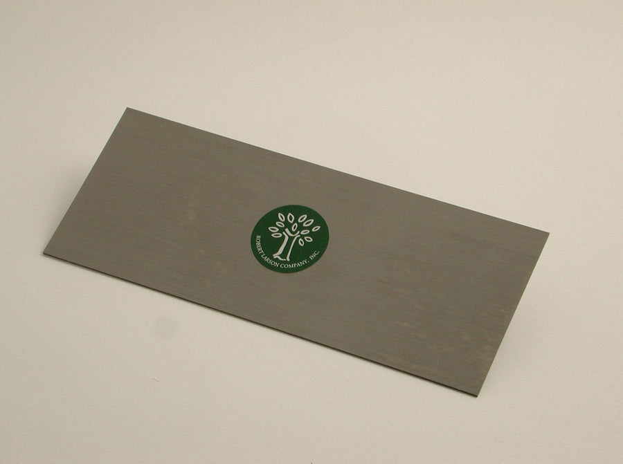 The Cabinet Scraper by ROB is a rectangular metal tool featuring a green circular sticker with a tree logo and the text "Brookstone Company Inc.," suggesting craftsmanship similar to German steel for durability and precision.