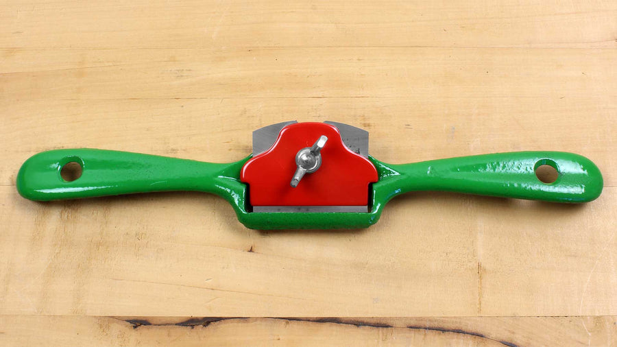 A green and red ROB Kunz Spokeshave Light Duty No 64 with a fine German steel blade rests on light wood. This two-handled tool is perfect for shaping and smoothing wood in various woodworking projects.