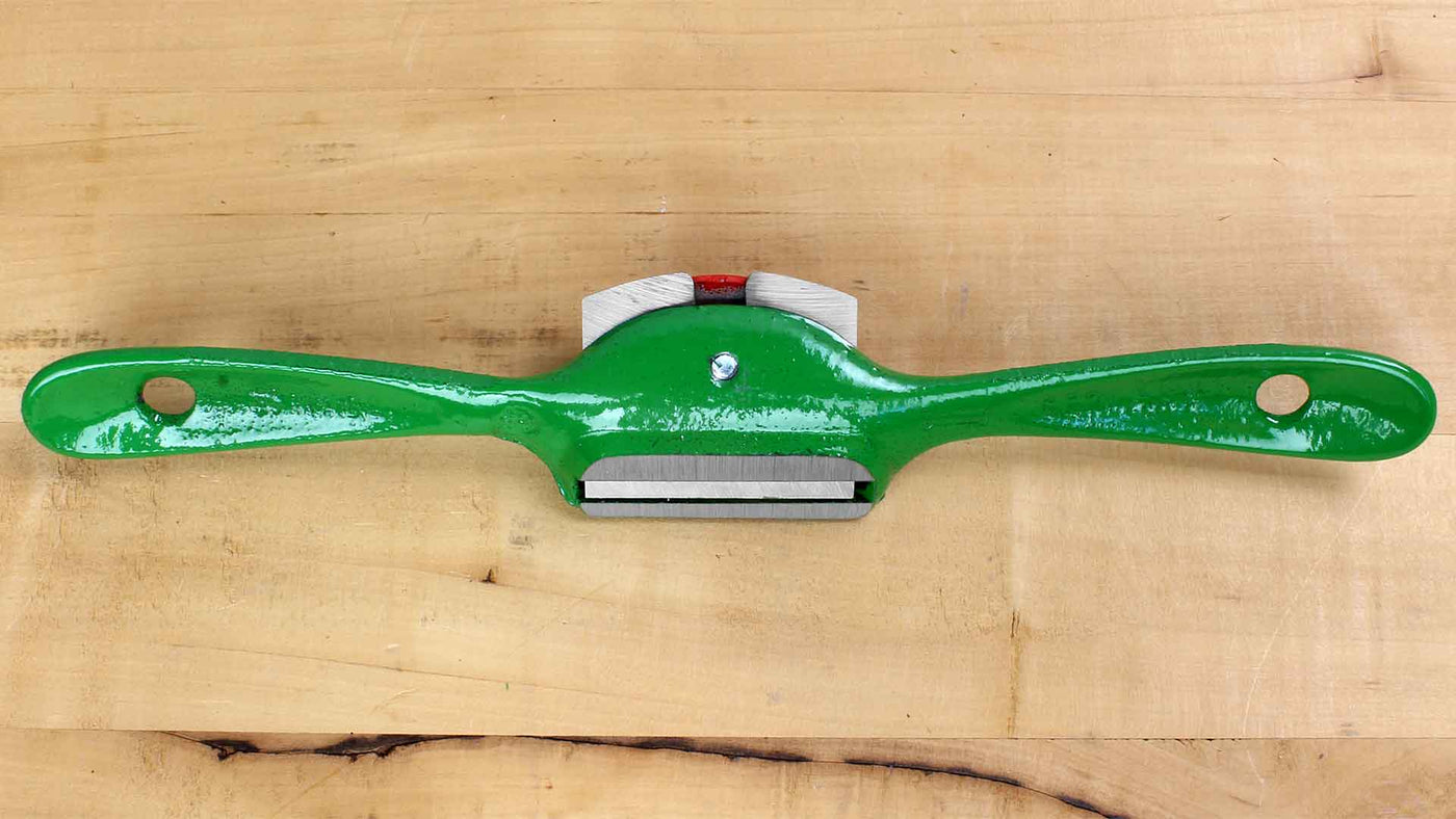 A green ROB Kunz Spokeshave Light Duty No 64 with a fine German steel blade and two curved handles rests on a light wooden surface, ideal for shaping and smoothing wood in woodworking projects.