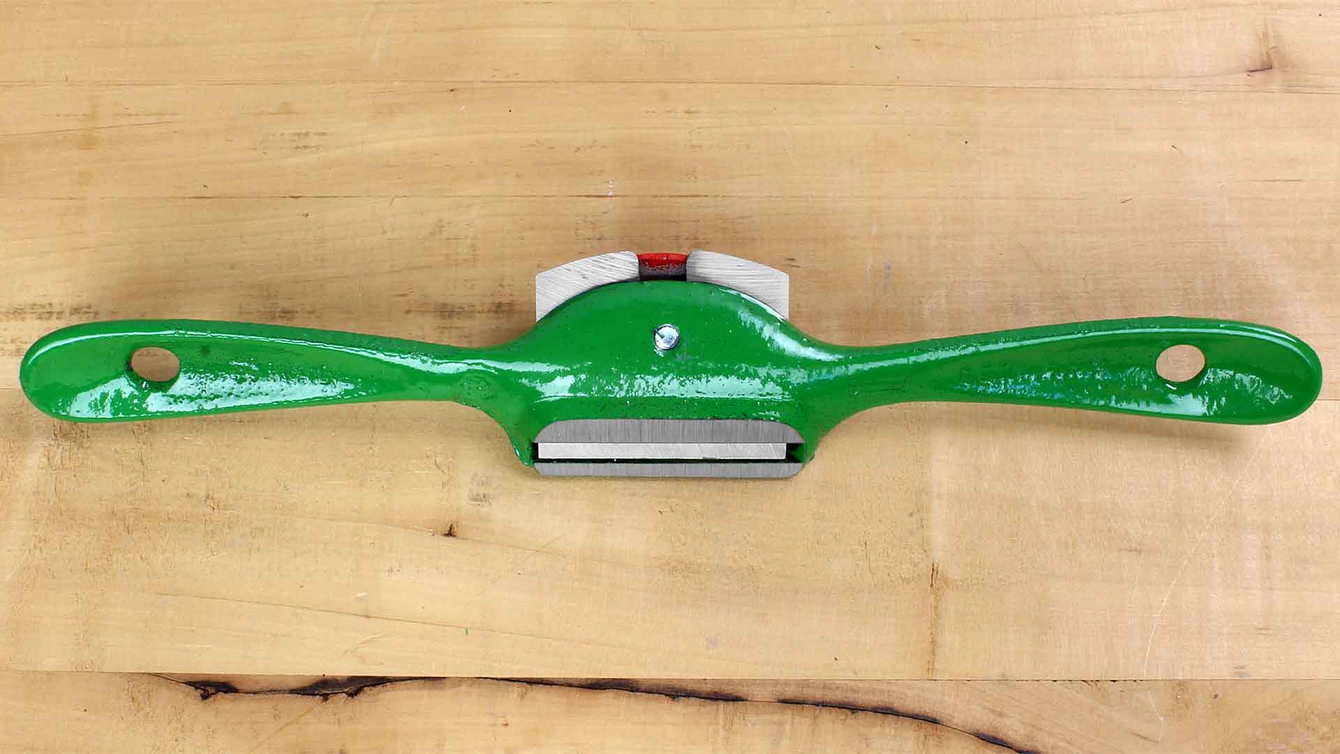 A green ROB Kunz Spokeshave Light Duty No 64 with a fine German steel blade and two curved handles rests on a light wooden surface, ideal for shaping and smoothing wood in woodworking projects.