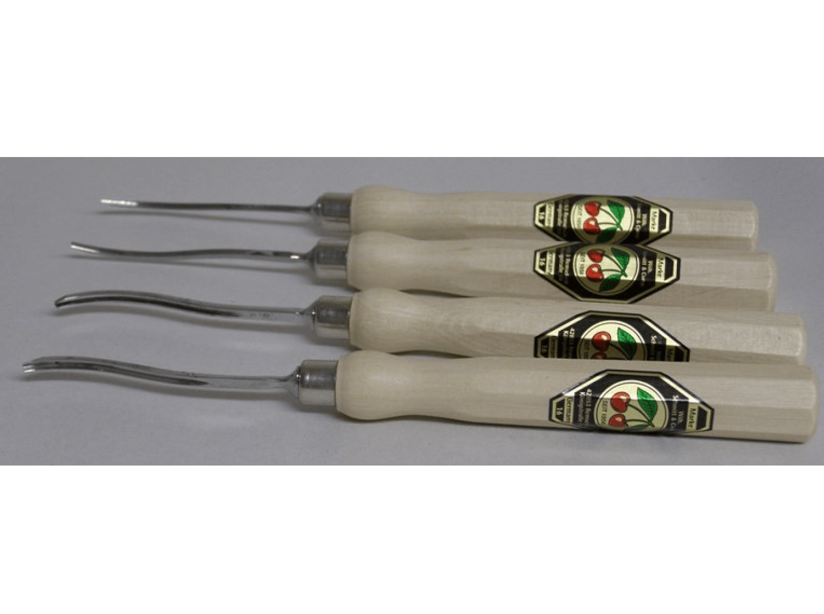 The ROB Two Cherries Micro Carving Tool Set of 4 features hornbeam wood handles with green and gold labels, each fitted with curved metal blades, arranged side by side.