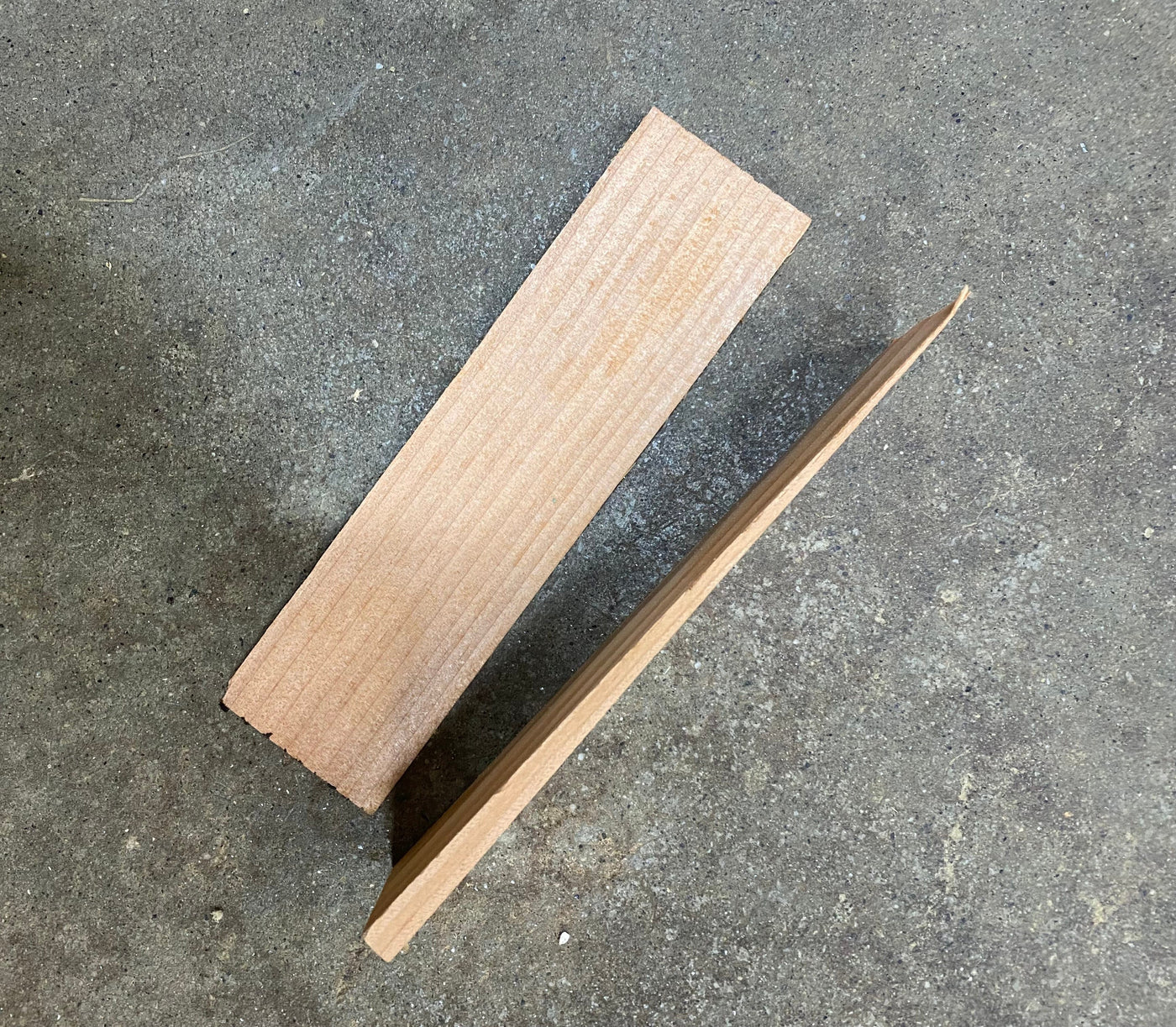 Two Shelter Institute Dovetail Shims are placed on a rough concrete surface—one flat, one upright—making them perfect for timber frame projects or fine-tuning dovetail floor joists.