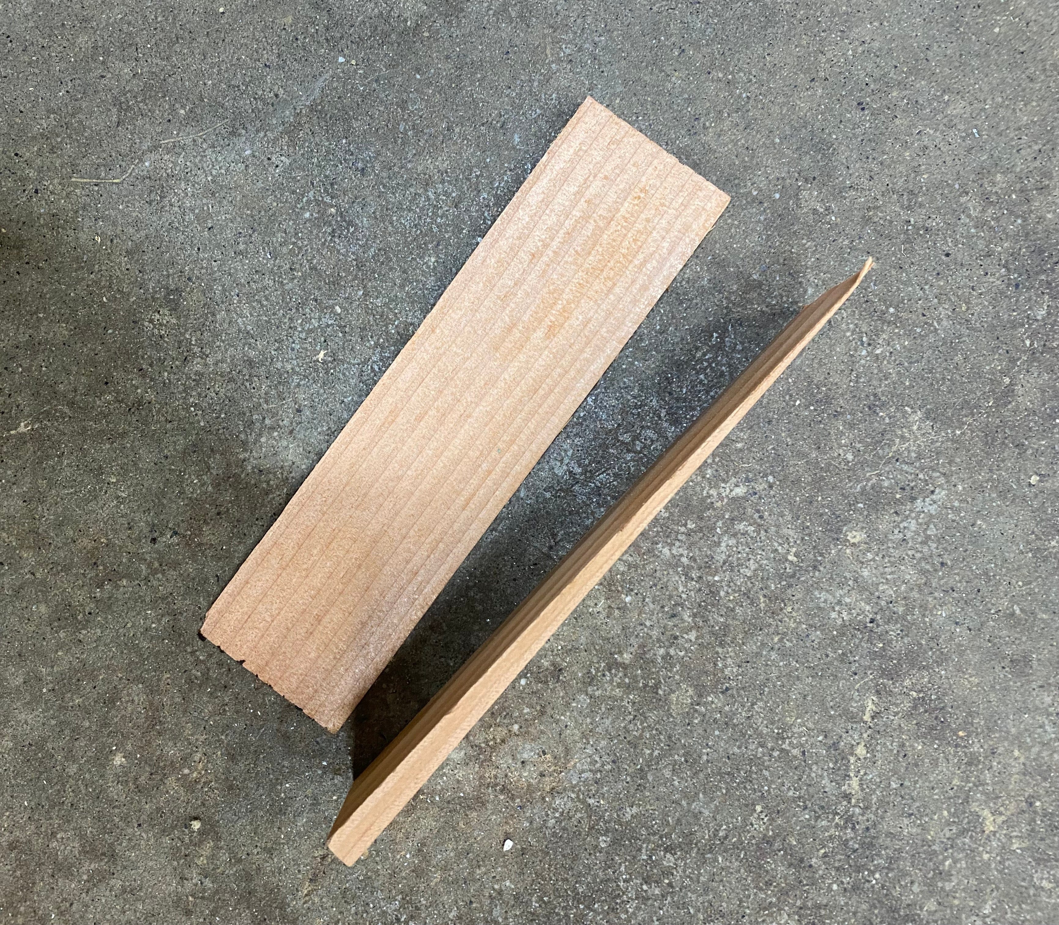 Two Shelter Institute Dovetail Shims are placed on a rough concrete surface—one flat, one upright—making them perfect for timber frame projects or fine-tuning dovetail floor joists.