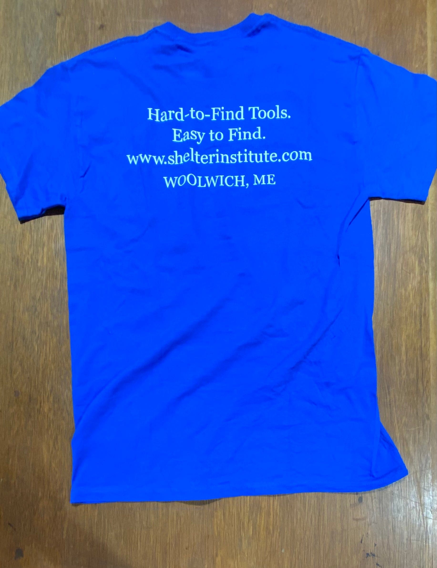 Introducing the Shelter Tools T-Shirt by Shelter Institute: a royal blue t-shirt featuring screen-printed white text on the back that reads "Hard-to-Find Tools. Easy to Find. www.shelterinstitute.com WOOLWICH, ME". Crafted from 100% cotton for exceptional comfort and durability.