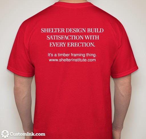 Back view of a person wearing a red Satisfaction T-shirt from Shelter Institute, featuring white text that reads, "SHELTER DESIGN BUILD SATISFACTION WITH EVERY ERECTION. It's a timber framing thing. www.shelterinstitute.com.