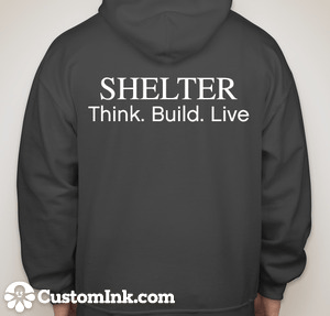 A person wearing a dark, lightweight Shelter Sweatshirt with "SHELTER Think. Build. Live" printed on the back. The logo "Shelter Institute" is visible at the bottom left of the poly/cotton blend hoodie.