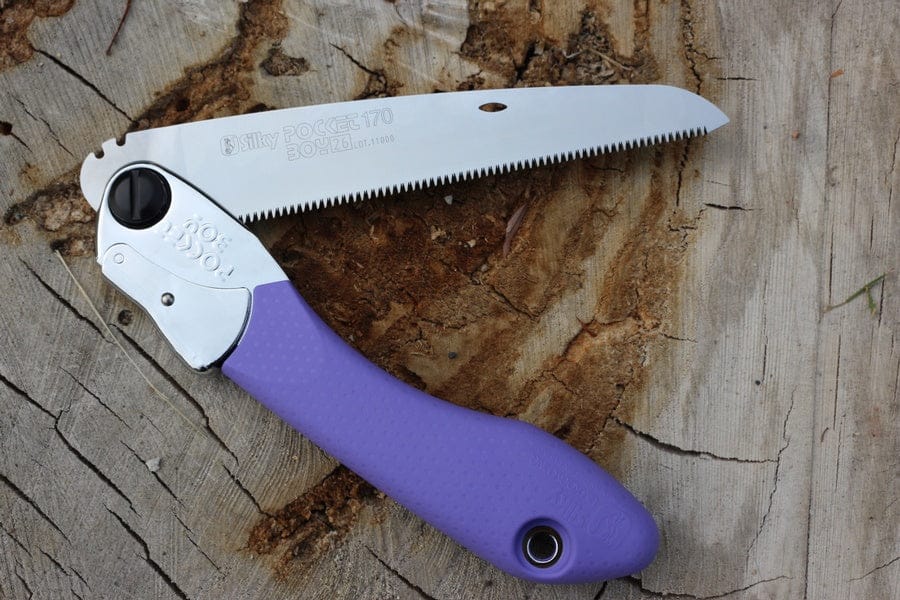 The BBT Pocket Boy 170 Folding Saw, featuring a tactile grip and purple handle, sits on a tree stump, highlighting its serrated blade and robust locking mechanism.