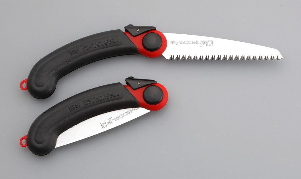 Two SHT Silky Accel 160 folding saws, in black and red, rest on a gray surface—one lightweight saw has its sharp-toothed blade extended, while the other’s blade is securely folded into the handle.