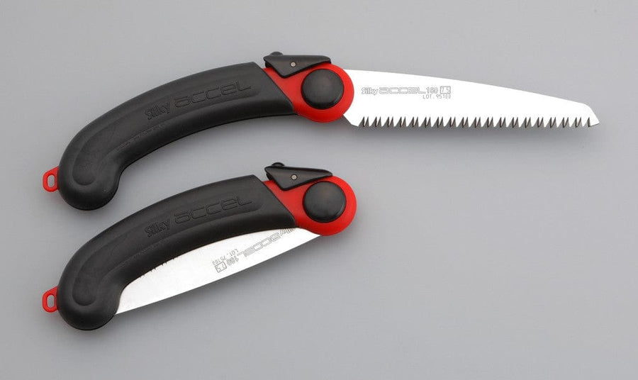 Two SHT Silky Accel 160 folding saws, in black and red, rest on a gray surface—one lightweight saw has its sharp-toothed blade extended, while the other’s blade is securely folded into the handle.