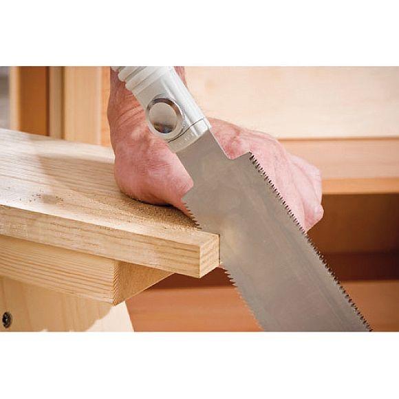 A hand uses the SHT Silky Hibiki Ryoba Handsaw with impulse-hardened teeth to cut light-colored wood, sawdust collecting near the cut, in what looks like an indoor workshop.