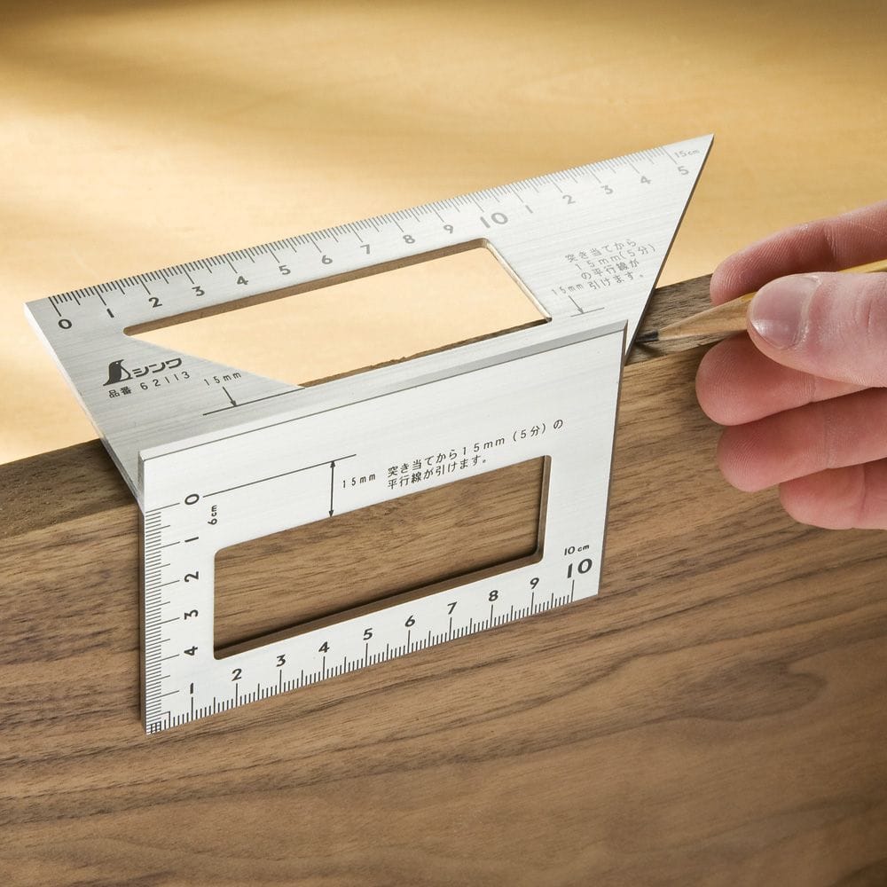 A person is using the SHWA Miter Rule on wood. This stainless steel tool from Shinwa provides precise measurements with multiple rulers and angles, perfect for timber framing projects.
