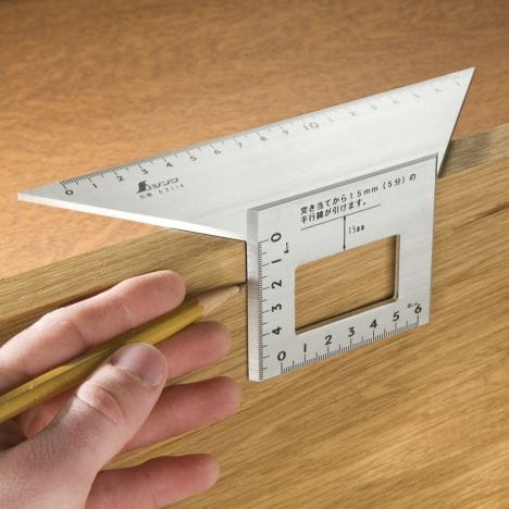 A person uses the SHWA Miter Rule by Shinwa to measure a wooden board, holding a pencil for precise cutting and marking.