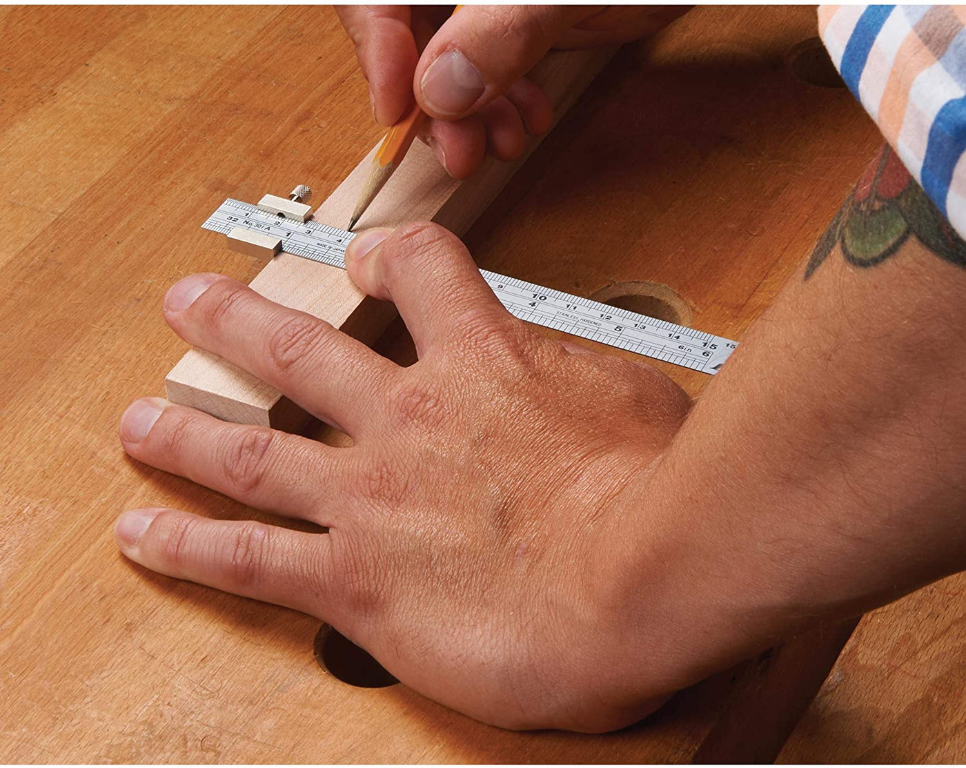 A person is using a caliper to measure wood on a workbench, marking points with a pencil. A SHWA 6-in Stainless Steel Ruler Metric and Inch, featuring a non-glare coating, sits nearby to ensure accuracy.