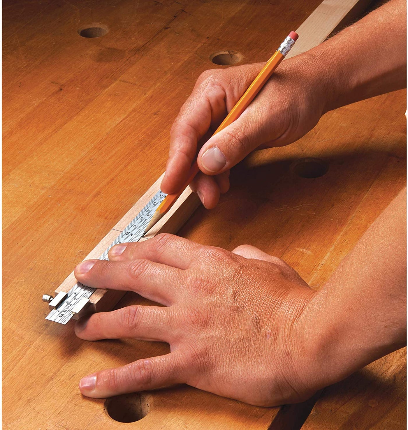 A person uses a marking gauge and pencil alongside the SHWA 6-in Stainless Steel Ruler Metric and Inch to measure and mark wood on a wooden workbench.