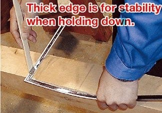 Close-up of someone using the SHWA Traditional Japanese Flexible Carpenter Square on wood, highlighting its thick edge for stability. The etched graduations provide precise metric and inch measurements seamlessly blended together.