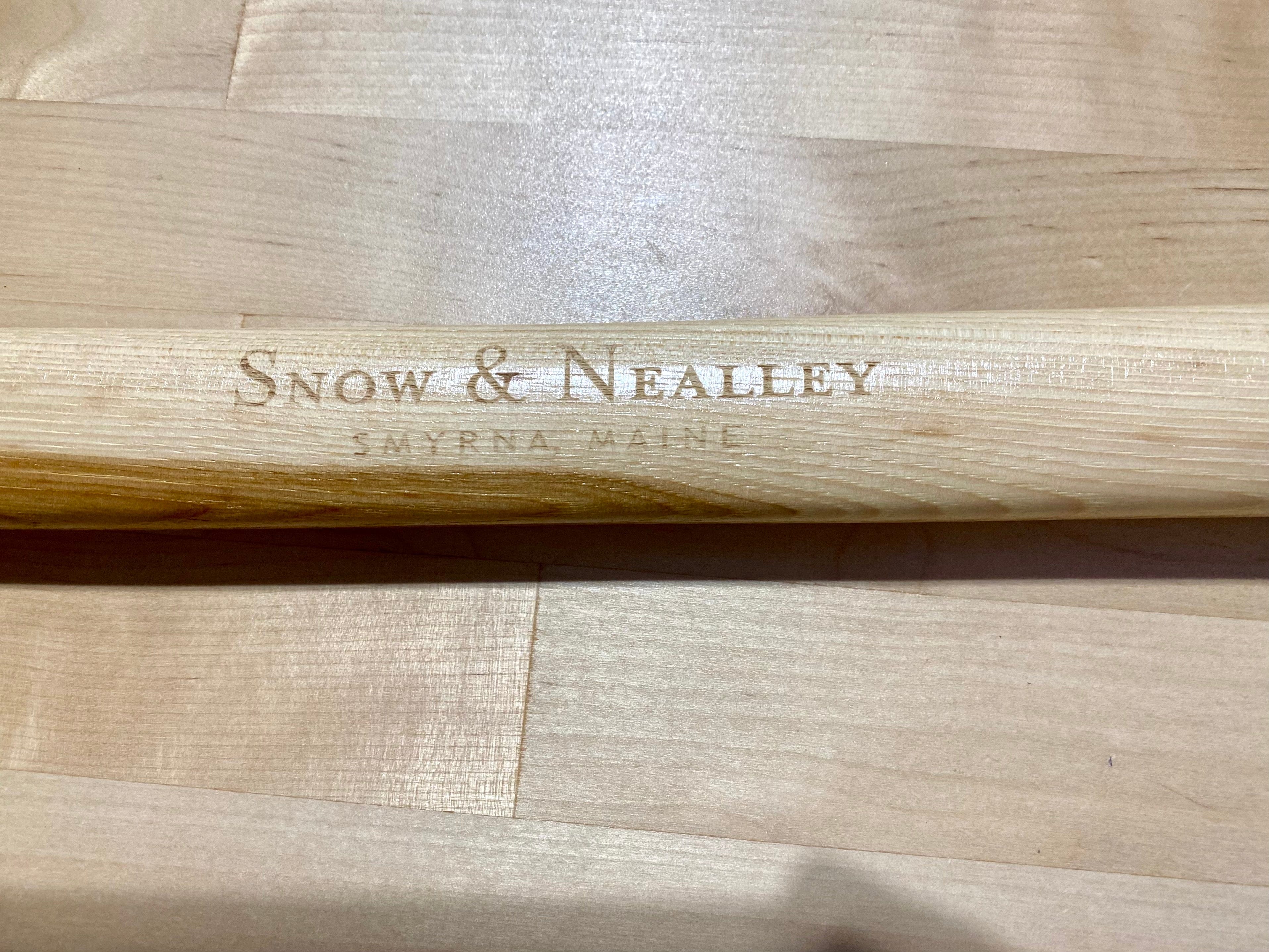 Close-up of the Snow & Nealley Pen Bay Kindling Axe by SNO, featuring an American hickory handle engraved with "Snow & Nealley Smyrna Maine," resting on a wooden surface.