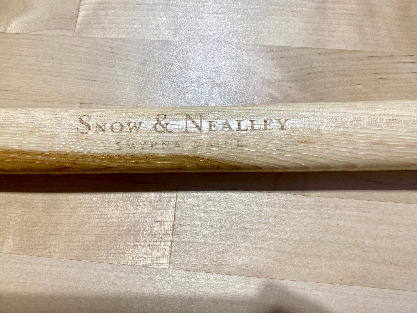 A wooden handle engraved with "Snow & Nealley, Smyrna Maine," perfect for outdoor enthusiasts seeking high-quality tools like the SNO Snow & Nealley Hudson Bay Camping Axe.