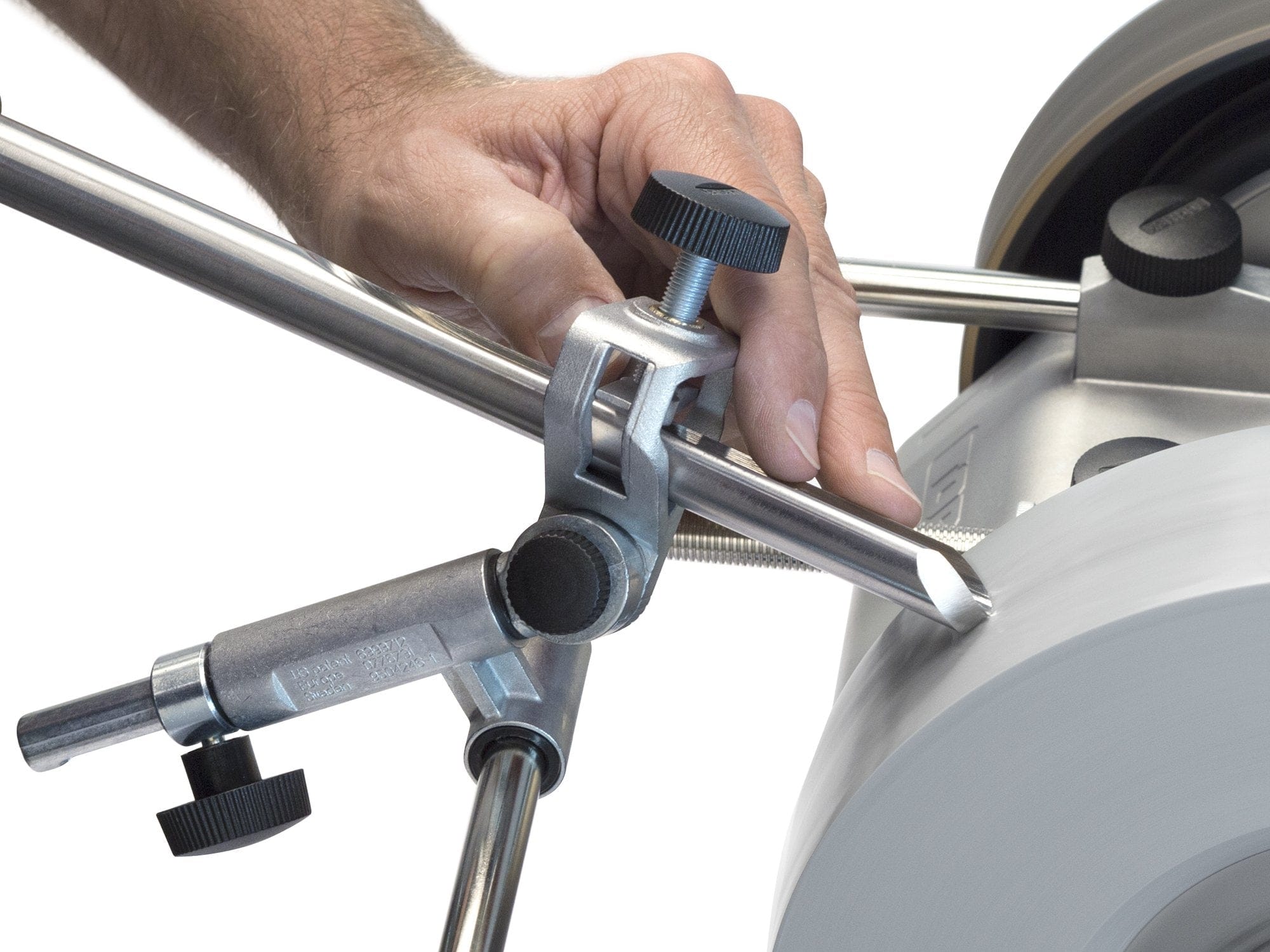 A hand adjusts a woodturning tool held in the TOR Tormek Gouge Jig against a rotating wheel, demonstrating precise edge sharpening.