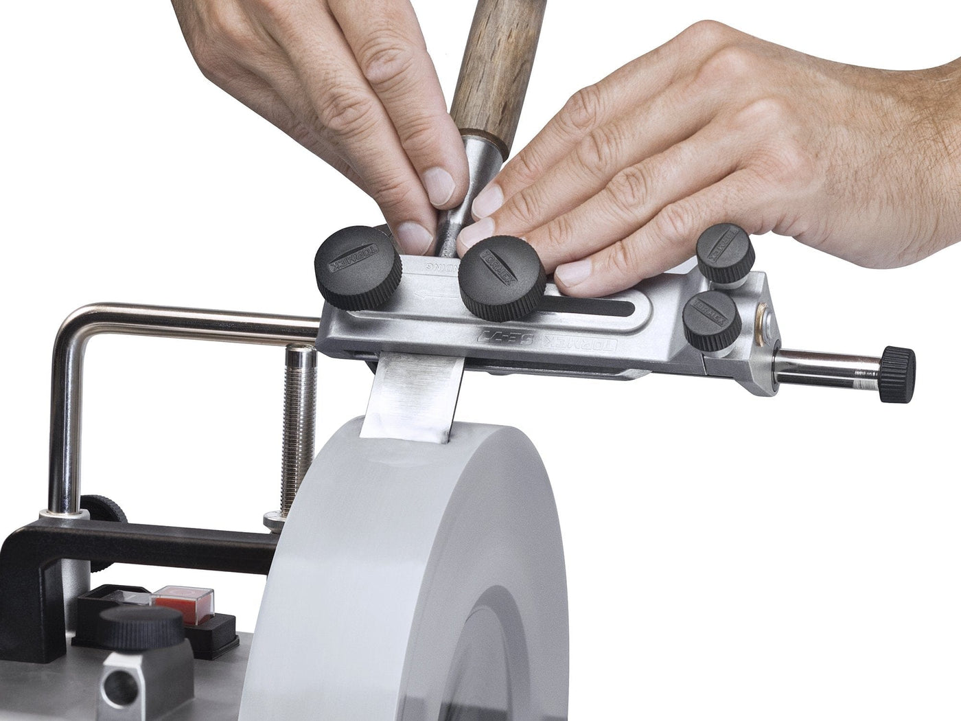 A user sharpens a tapered chisel with the TOR Tormek Square Edge Jig and a rotating sharpening stone, adjusting the tool for precise alignment.
