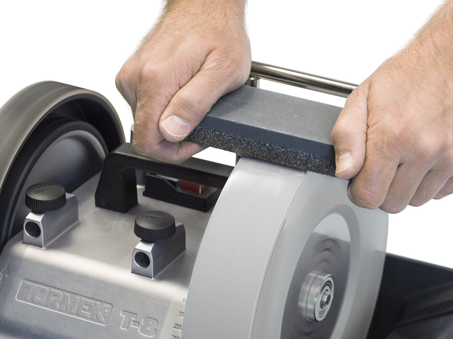 Close-up of hands using the TOR Tormek Stone Grader to sharpen and condition the grindstone on a Tormek T-8 water-cooled sharpening machine.