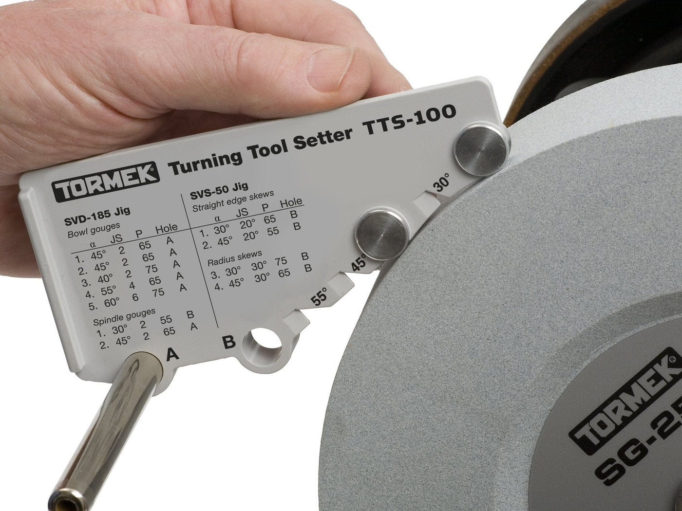 A hand uses the TOR Tormek Turning Tool Setter against a grinding wheel, aligning it with angle settings to precisely sharpen woodturning gouges as shown in the diagram.