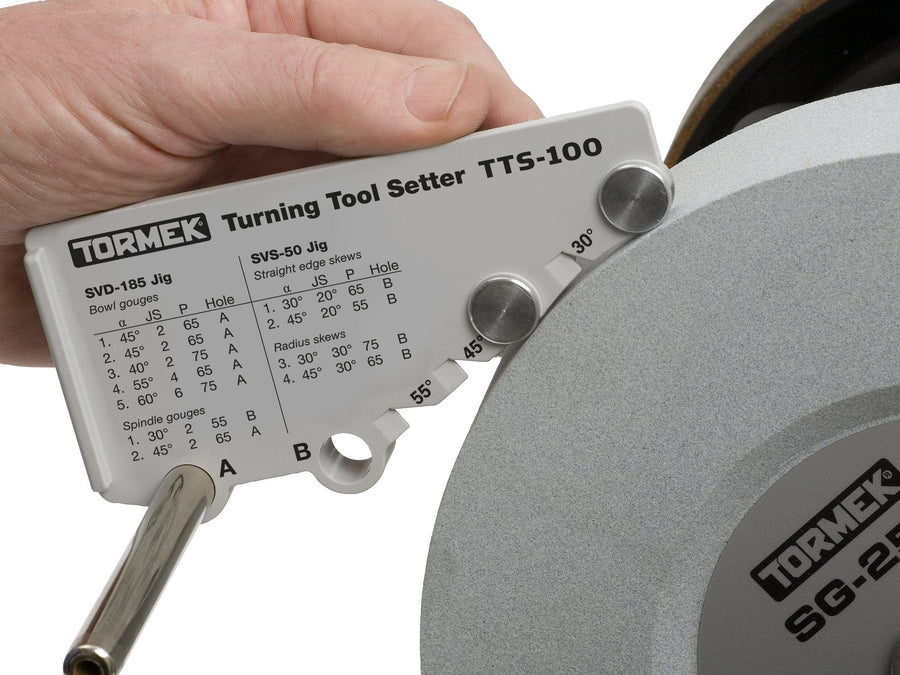 A hand uses the TOR Tormek Turning Tool Setter against a grinding wheel, aligning it with angle settings to precisely sharpen woodturning gouges as shown in the diagram.