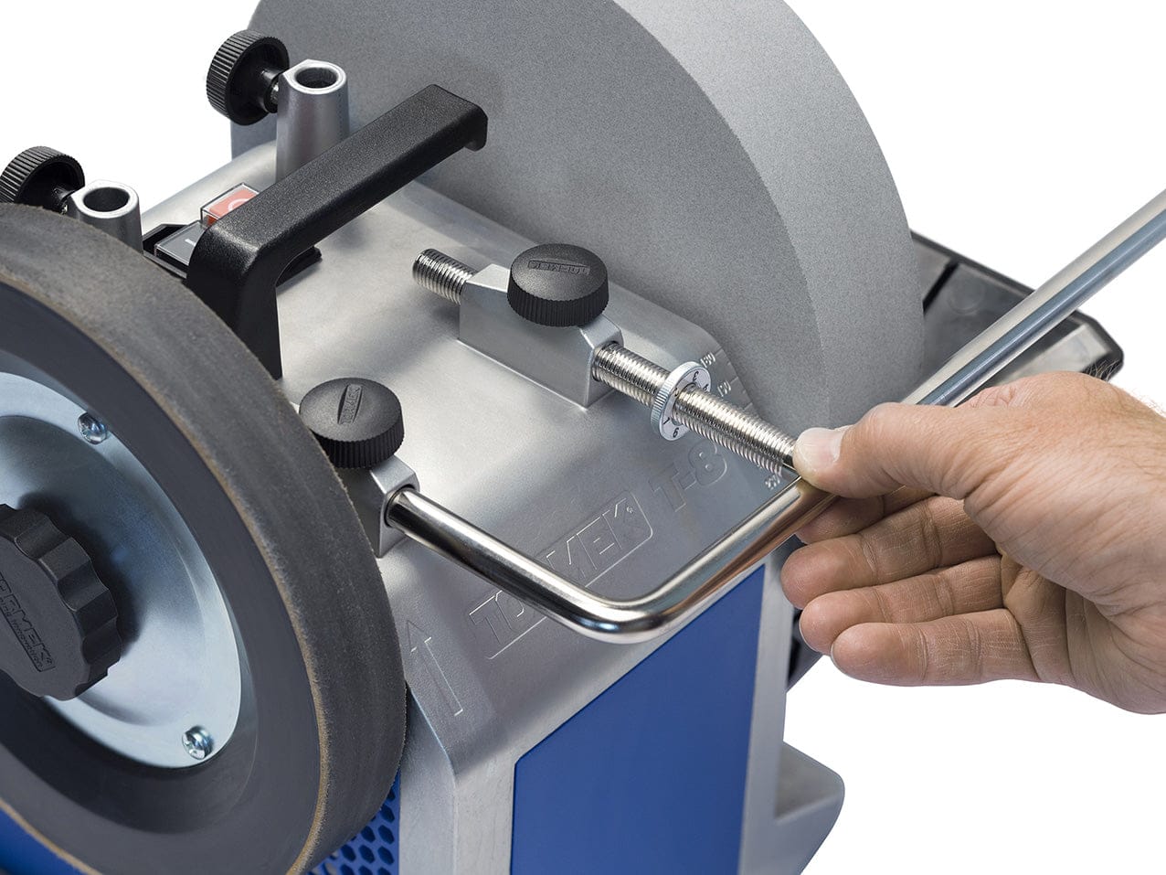 A close-up of a hand fine-tuning a metal rod using the TOR Universal Support with Micro Adjustment T-4/T-8, adjusting the grinding wheel and knobs for precise sharpening.