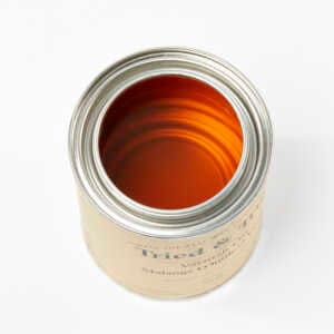 An open can of Tried & True Varnish Oil Finish by TRD, its amber-colored liquid gleaming against the metallic rim, viewed from above, rests on a white background.