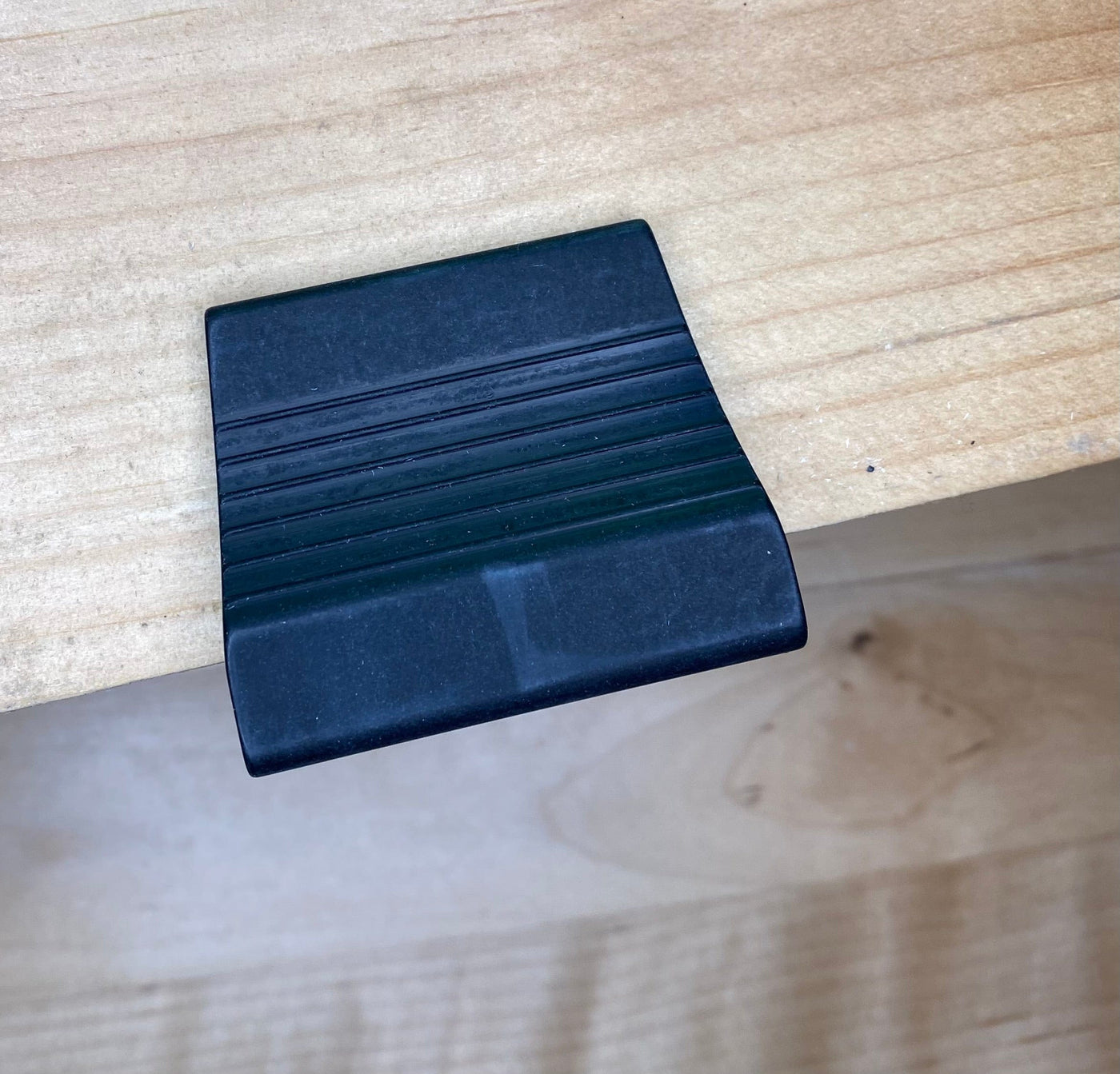 The VERITAS DOVETAIL SADDLE MARKER from VER features a precision-machined, black, rectangular rubber grip designed to be placed over the edge of a light wooden surface.