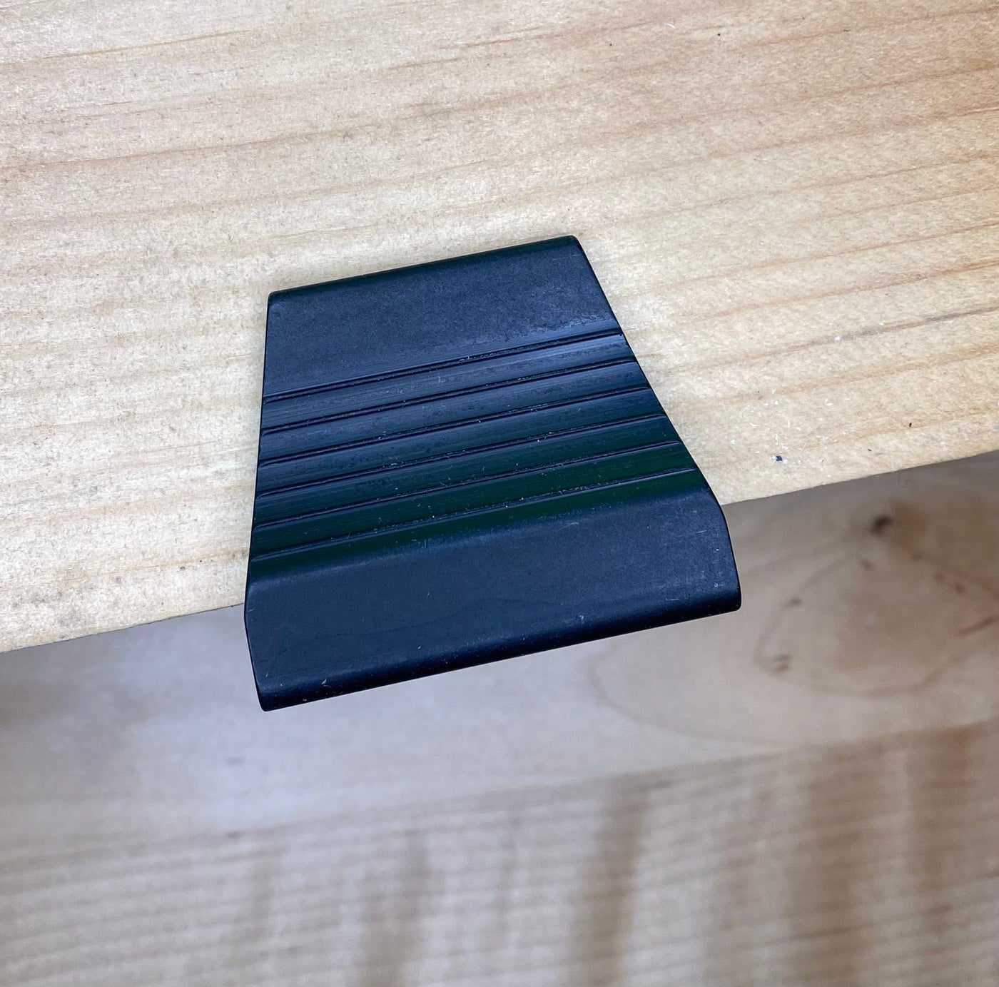 A VERITAS DOVETAIL SADDLE MARKER from the brand VER, made of black plastic and featuring ridges similar to a precision-machined tool, rests on a wooden surface.